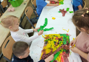 Dzieci malują bibułą, tworząc tło do dalszego etapu pracy.
