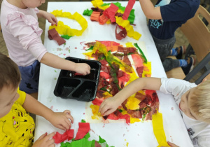 Dzieci malują bibułą, tworząc tło do dalszego etapu pracy.