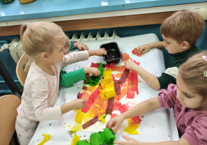 Dzieci malują bibułą, tworząc tło do dalszego etapu pracy.