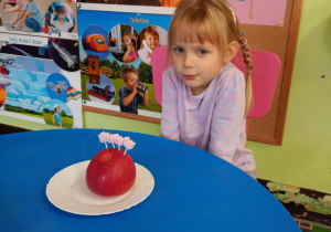 Dziewczynka siedzi przy urodzinowym torcie z jabłuszka.