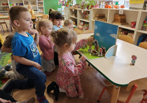 Dzieci słuchają bajki o trzech świnkach, kolejno podchodzą i dokładają rekwizyty na scenę.