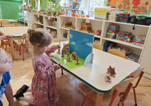 Dzieci słuchają bajki o trzech świnkach, kolejno podchodzą i dokładają rekwizyty na scenę.