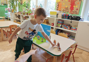 Dzieci słuchają bajki o trzech świnkach, kolejno podchodzą i dokładają rekwizyty na scenę.