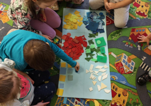 Dzieci podzielone na dwie grupy układają figury geomeryczne na poszczególnych polach wg określonych cech.