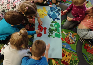 Dzieci podzielone na dwie grupy układają figury geomeryczne na poszczególnych polach wg określonych cech.