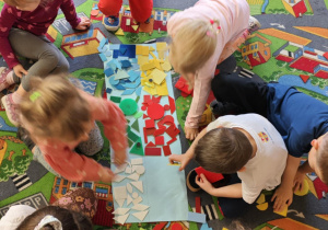 Dzieci podzielone na dwie grupy układają figury geomeryczne na poszczególnych polach wg określonych cech.