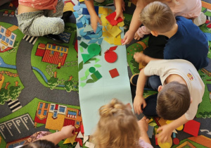 Dzieci podzielone na dwie grupy układają figury geomeryczne na poszczególnych polach wg określonych cech.