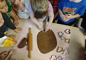 Dzieci za pomocą foremek wycinają z ciasta pierniki.
