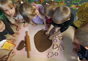 Dzieci za pomocą foremek wycinają z ciasta pierniki.