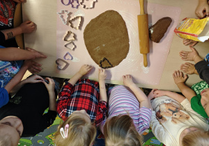 Dzieci za pomocą foremek wycinają z ciasta pierniki.