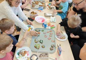 Dzieci wraz z Rodzicami ozdabiają pierniczki na świąteczny kiermasz.