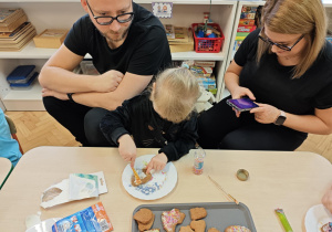 Dzieci wraz z Rodzicami ozdabiają pierniczki na świąteczny kiermasz.