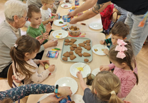 Dzieci wraz z Rodzicami ozdabiają pierniczki na świąteczny kiermasz.