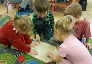 Dzieci w ryżu odwzorowują odszukane w nim figury geometryczne.