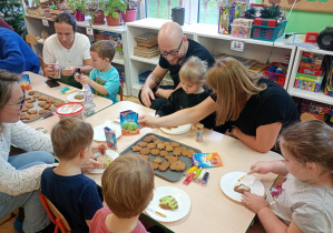 Rodzice z dziećmi ozdabiają pierniczki na świąteczny kiermasz.