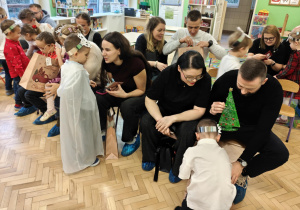 Dzieci wręczają rodzicom samodzielnie wykonane prezenty - stroik w kształcie choinki.