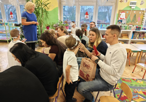 Dzieci wręczają rodzicom samodzielnie wykonane prezenty - stroik w kształcie choinki.