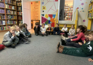 Dzieci siedzą na dywanie w bibliotece i słuchają opowiadania o tematyce świątecznej.