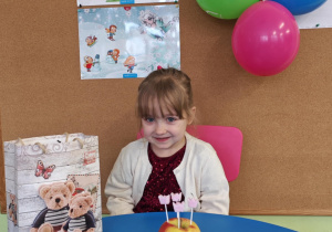 Dziewczynka siedzi przy urodzinowym stoliku.