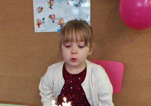 Dziewczynka zdmuchuje świeczki na urodzinowym torcie.