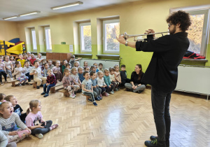 Dzieci słuchają dźwięków wygrywanych na trąbce.