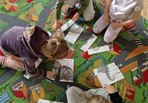 Dzieci w małych zespołach układają pocięte obrazki z dinozaurami.