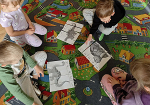 Dzieci w małych zespołach układają pocięte obrazki z dinozaurami.