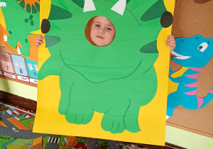 Dziecko pozuje do zdjęcia w ramce dinozaura.