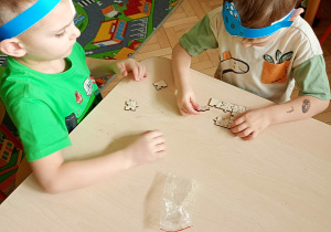 Dzieci ukłądają drewniane puzzle z dinozaurami.