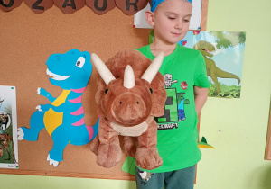 Dziecko pozuje do zdjęcia z dinozaurem pluszakiem.