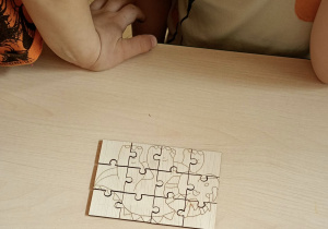 Dzieci ukłądają drewniane puzzle z dinozaurami.
