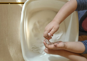 Dziecko poszukuje ukrytych przedmiotów w pojemniku z mąką.