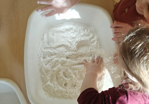 Dziecko poszukuje ukrytych przedmiotów w pojemniku z mąką.