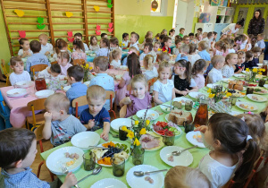 Dzieci siedzą przy złączonych stołach i czekają na świąteczny barszczyk.