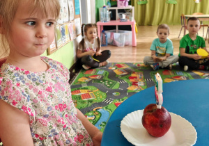 Dziewczynka siedzi przy stole, na którym została zapalona urodzinowa świeczka.