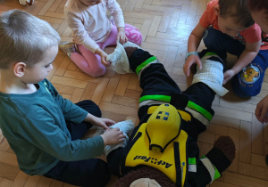Dzieci ćwiczą umiejętność owinięcia rany bandażem.