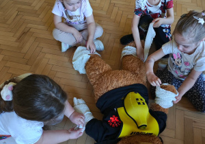 Dzieci ćwiczą umiejętność owinięcia rany bandażem.