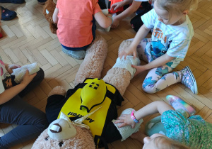 Dzieci ćwiczą umiejętność owinięcia rany bandażem.