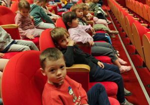 Dzieci siedzą w teatrze oczekując na spektakl.
