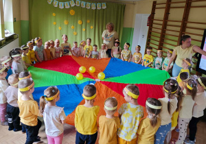 Dzieci bawią się z wykorzystaniem chusty animacyjnej i żółtych balonów.