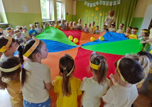 Dzieci bawią się z wykorzystaniem chusty animacyjnej i żółtych balonów.