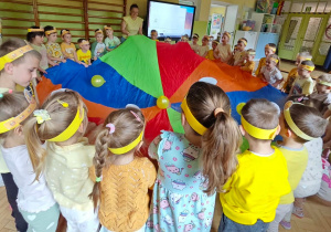 Dzieci bawią się z wykorzystaniem chusty animacyjnej i żółtych balonów.