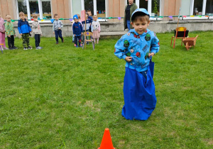 Dziecko pokonuje tor przeszkód, skacząc w worku.