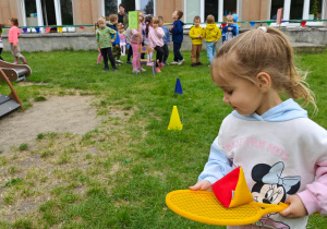 Dziecko slalomem omija pachołki, przenosząc woreczek na rakiecie tenisowej.