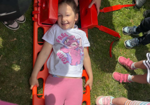Strażak Martyna pokazuje dzieciom, w jaki sposób zabezpiecza się rannego podczas transportu.