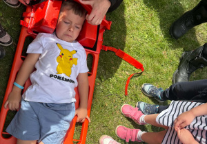 Strażak Martyna pokazuje dzieciom, w jaki sposób zabezpiecza się rannego podczas transportu.