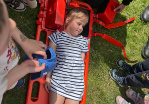 Strażak Martyna pokazuje dzieciom, w jaki sposób zabezpiecza się rannego podczas transportu.