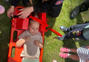 Strażak Martyna pokazuje dzieciom, w jaki sposób zabezpiecza się rannego podczas transportu.