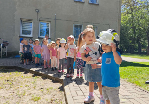 Dzieci przymierzają hełm strażacki.