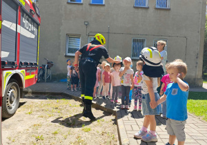 Dzieci przymierzają hełm strażacki.